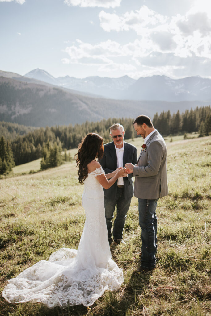 Couple exchanging rings on the side of a mountain at their micro wedding while their officiant marries them.