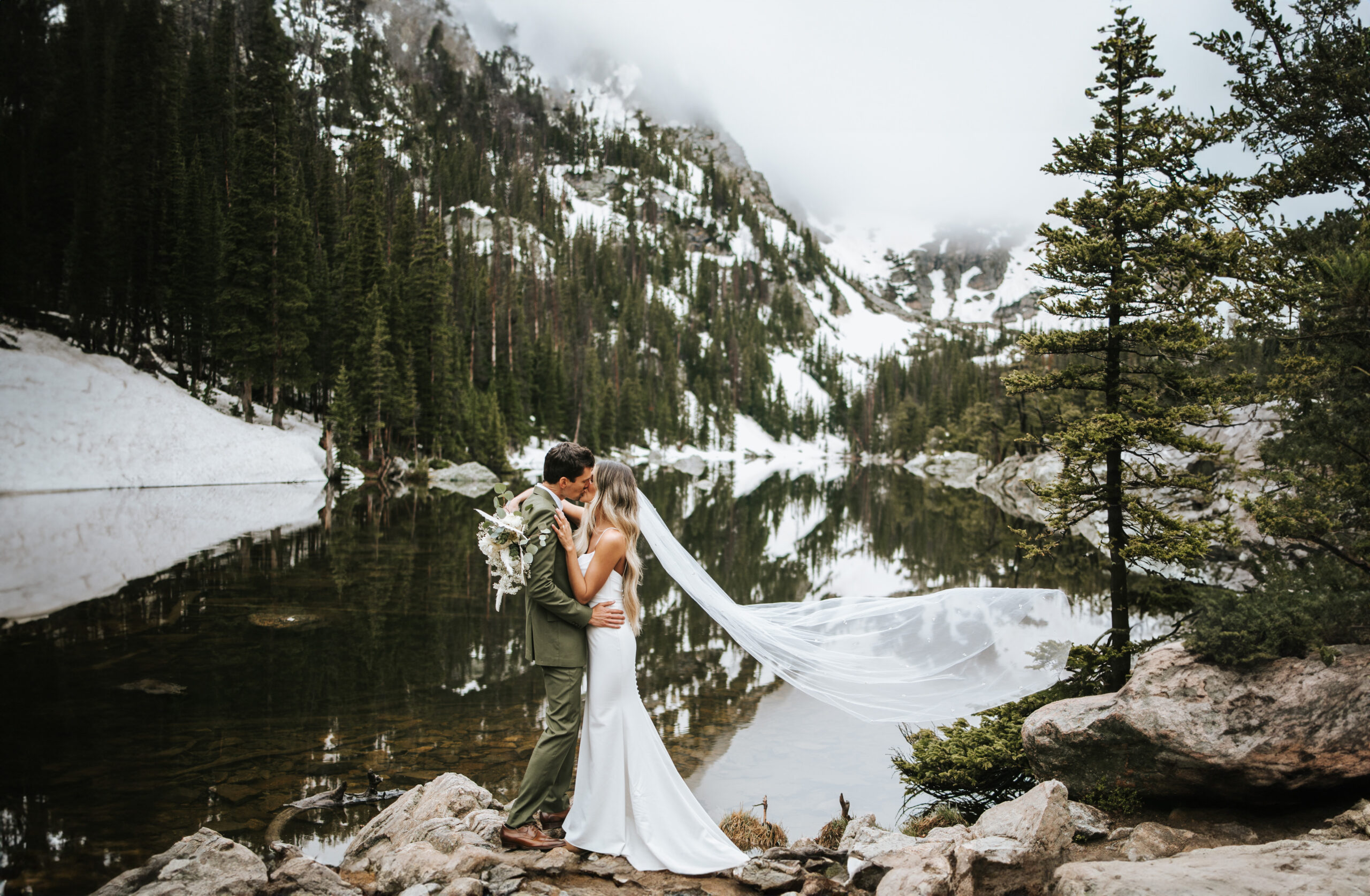 Couple kissing by an alpine lake on their elopement day.